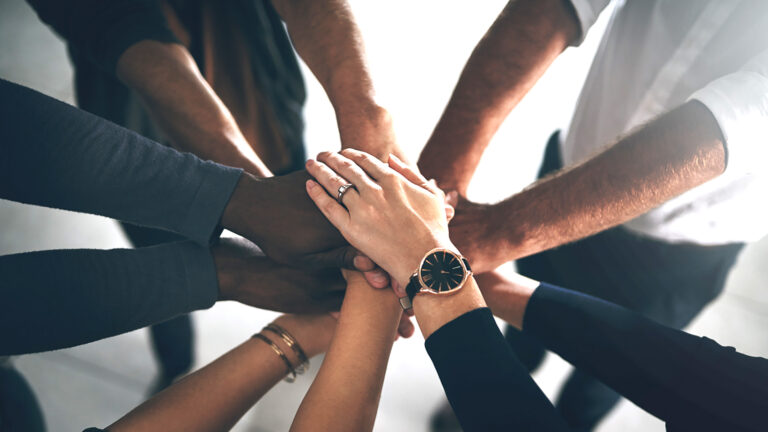 Cropped shot of a group of colleagues joining their hands in solidarity during a late night at work