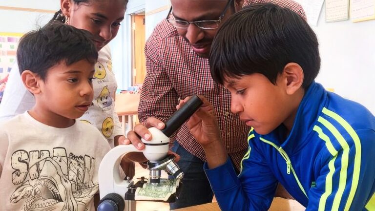 A Keck School staffer works with two youth on a microscope