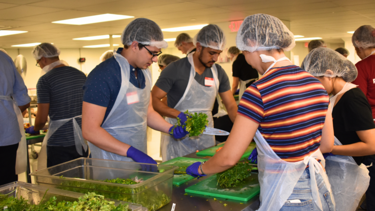 Group of students in hair nets and aprons cutting fresh veggies.