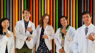 Five students making a shaka sign in front of a multi color background
