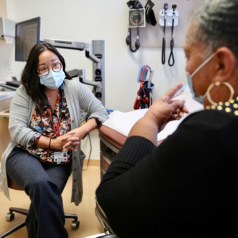 Masked family medicine physicians speaks to patient in a doctor's office visit.