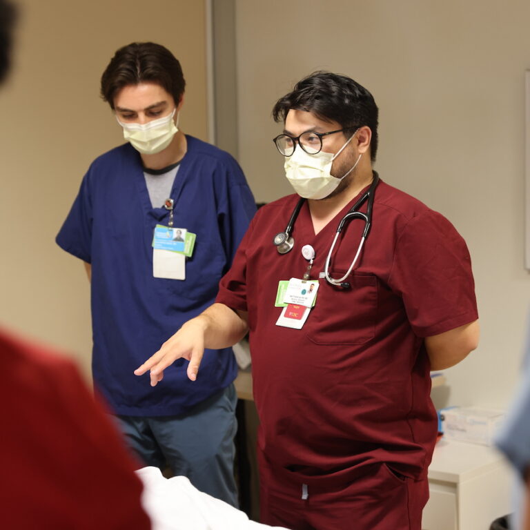 Residents in clinical skills lab in their scrubs having a conversation.