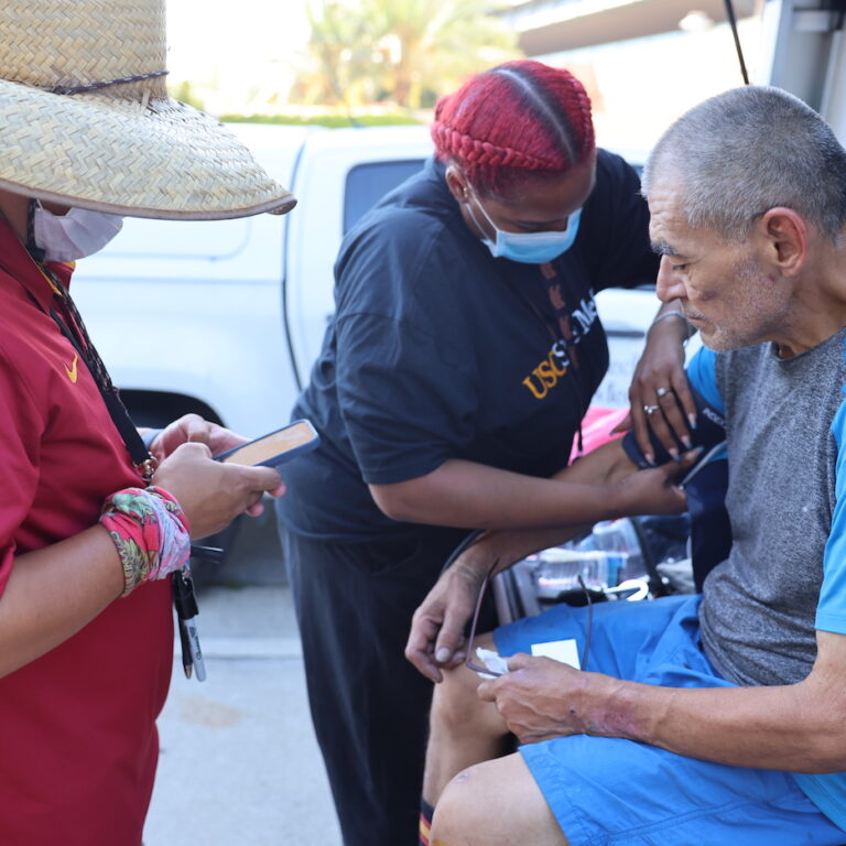 Patient gets blood pressure taken on the street by MA and nurse on Street Medicine.