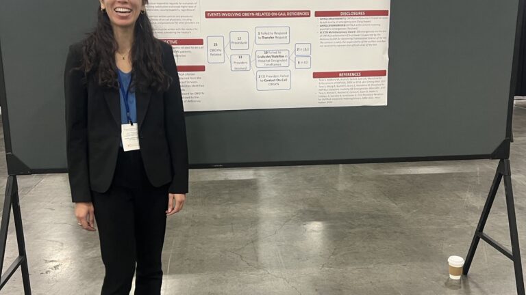 Medical student stands by scientific poster at a conference