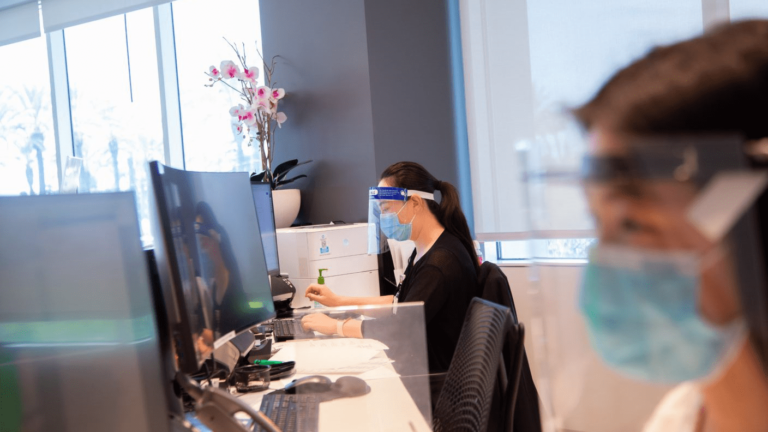 Two health care workers in face masks at a desk.