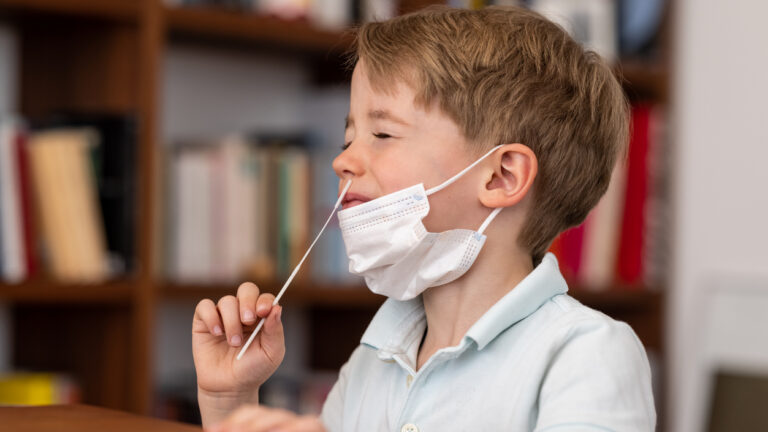 4 year pre-school boy introduces a corona test swab into his nose as he carries out a corona self test