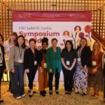 Group of nine people stand in front of banner at conference event