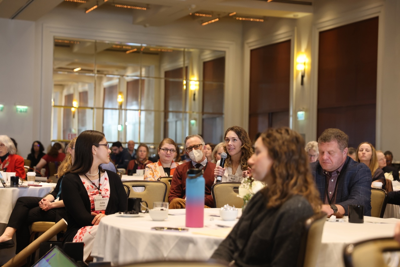 Women holds microphone to ask question in room full of people at conference
