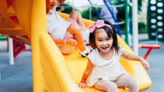 Two young girls play on a slide in a park.
