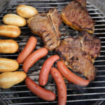 Photo shows steaks and hot dogs on a grill.