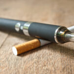 Closeup of black E-cigarette with cigarette on wooden background