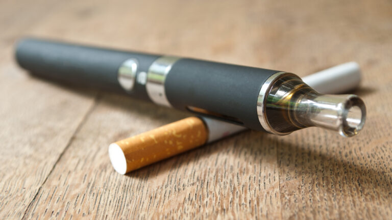 Closeup of black E-cigarette with cigarette on wooden background