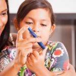 Photo shows mother helping child with type 1 diabetes monitor her blood sugar.