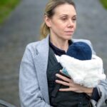 Photo shows woman holding baby staring off into the distance.