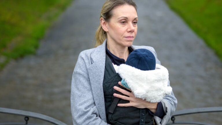 Photo shows woman holding baby staring off into the distance.
