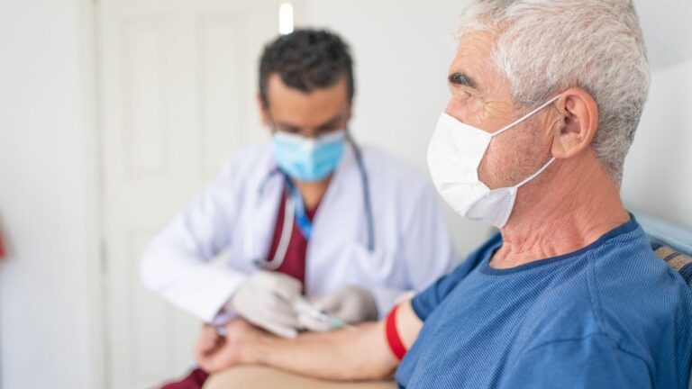 Photo shows health worker taking blood sample from middle-aged man.