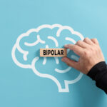 Image shows Hand puts a wooden block with the word bipolar on a human brain symbol.