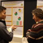 Resident speaks with faculty in front of research posters at 3rd Annual Family Medicine Research Day.