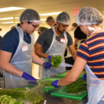 Group of students in hair nets and aprons cutting fresh veggies.