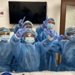 Group of children dressed in medical gowns, gloves, masks and hair nets and pose during a surgery lesson.