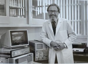 Image of Herb in a lab coat next to a computer