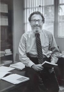 Image of Herb sitting on a desk holding a book