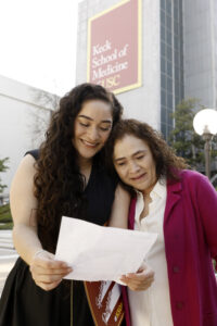 Student reads her match day results with her mother standing in front of the Keck School of Medicine banner