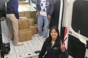 smiling young woman gives the Trojan "Fight On" while loading van with boxes