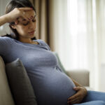 Tired stressed pregnant woman sitting on a couch and holding her belly