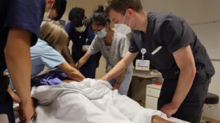 A group of resident students practicing on a mannequin in a skills lab