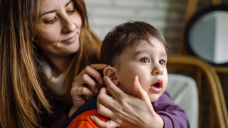 A woman gently holds a child's ear, possibly checking for an earache or providing comfort.
