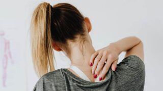 Woman in a ponytail grabbing the bottom of her neck indicating neck pain