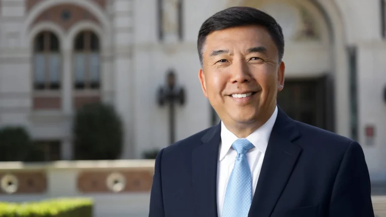 Yang Chai is dressed in a suit with a light blue tie posed in front of a building at USC.