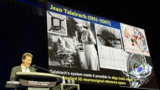 Photo shows Paul Thompson delivering the Talairach Lecture at OHBM 2025.