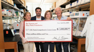 Four individuals hold up a large check to the USC Norris
