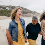 A group of four middle-aged women smiling and walking on the beach together