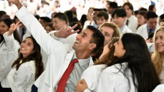 A group of people wearing white coats and ties, posing for a selfie at the White Coat ceremony.