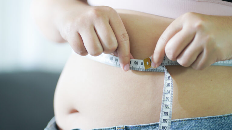 Obese girl touching her fat belly and measuring waist.
