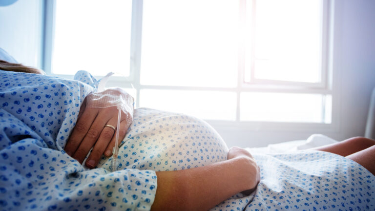Close-up of a pregnant woman's belly in the hospital bed with catheter in hand