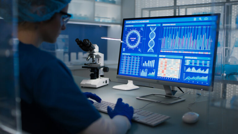 Female scientist in protective clothes and glasses looking at the computer screen. Researching diseases and DNA test results