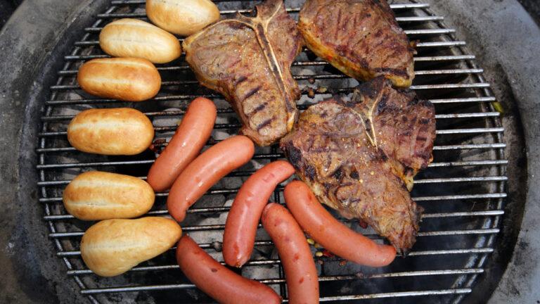 Photo shows steaks and hot dogs on a grill.